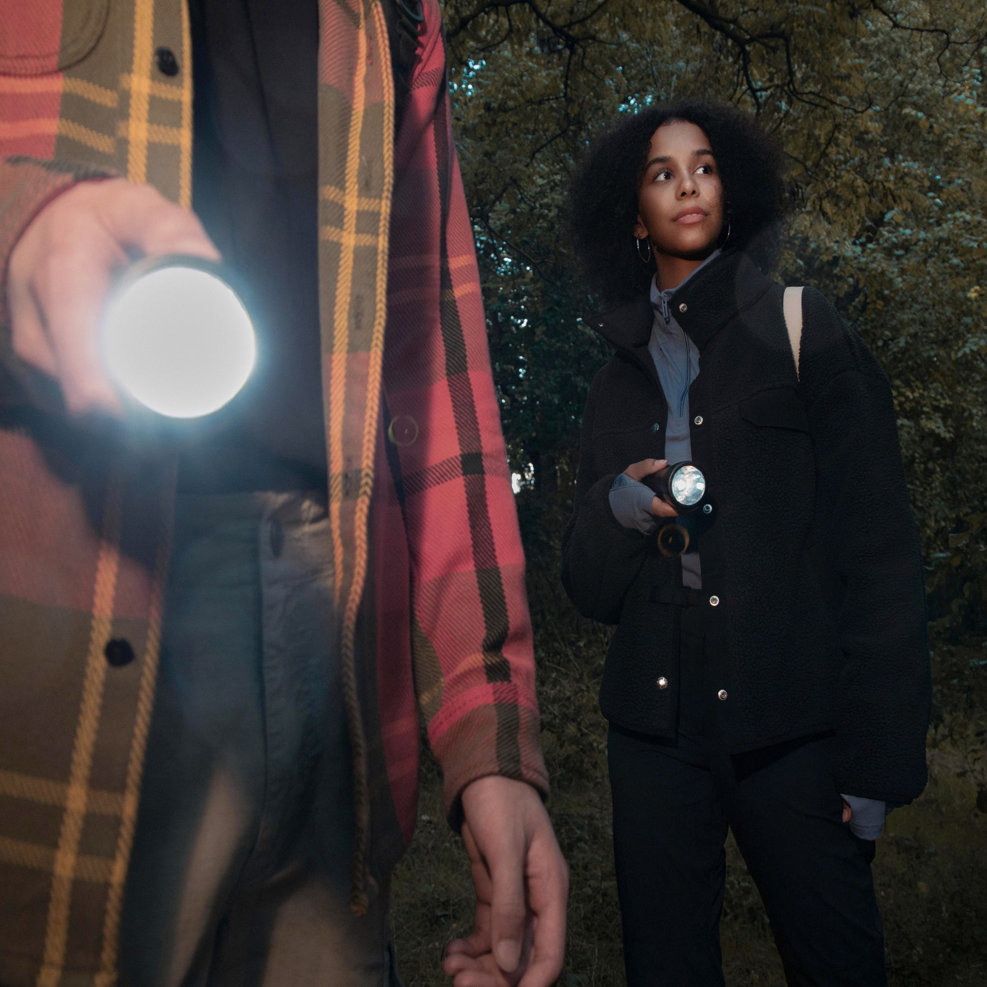 Abenteuer im Wald: Paar erlebt magische Momente mit WaterLamp-Taschenlampen. Mann im karierten Hemd hält leuchtende Taschenlampe, während die Frau ihre Lampe gen Wald leuchtet. Entdecke die Beleuchtung der Zukunft im WaterLamp Shop!